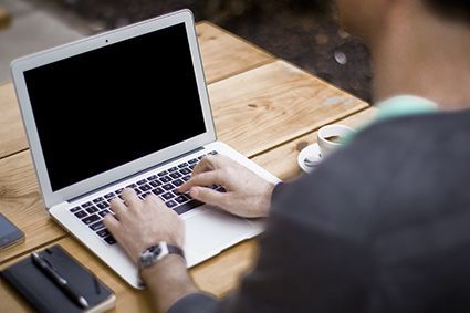 Ein Mann tippt an einem Holztisch auf einem Laptop.