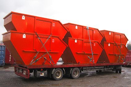 Auf einem Anhänger ist eine Reihe roter Müllcontainer übereinander gestapelt.