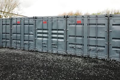 Auf einem Kiesplatz steht eine Reihe von Schiffscontainern.