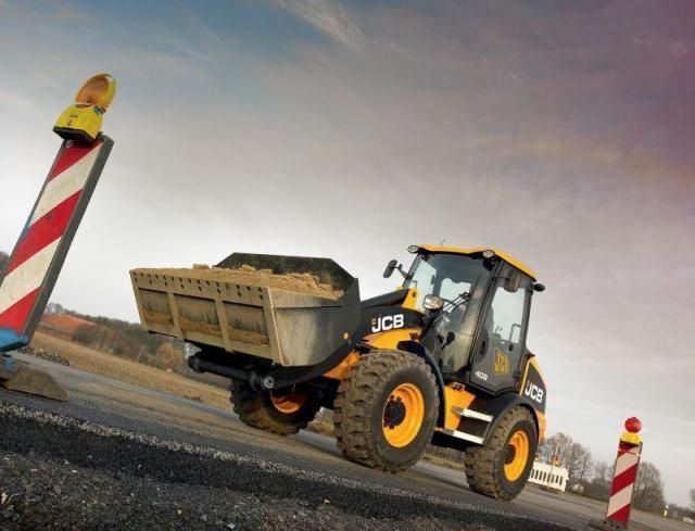 Ein gelb-schwarzer JCB-Traktor fährt eine Straße entlang