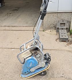 Eine blau-silberne Maschine steht auf dem Boden vor einer Garage.