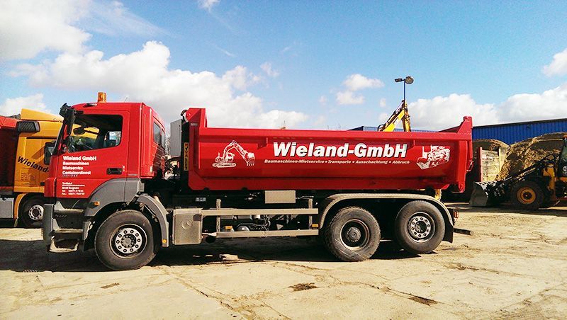 Ein roter Muldenkipper der Wieland GmbH steht auf einem unbefestigten Grundstück
