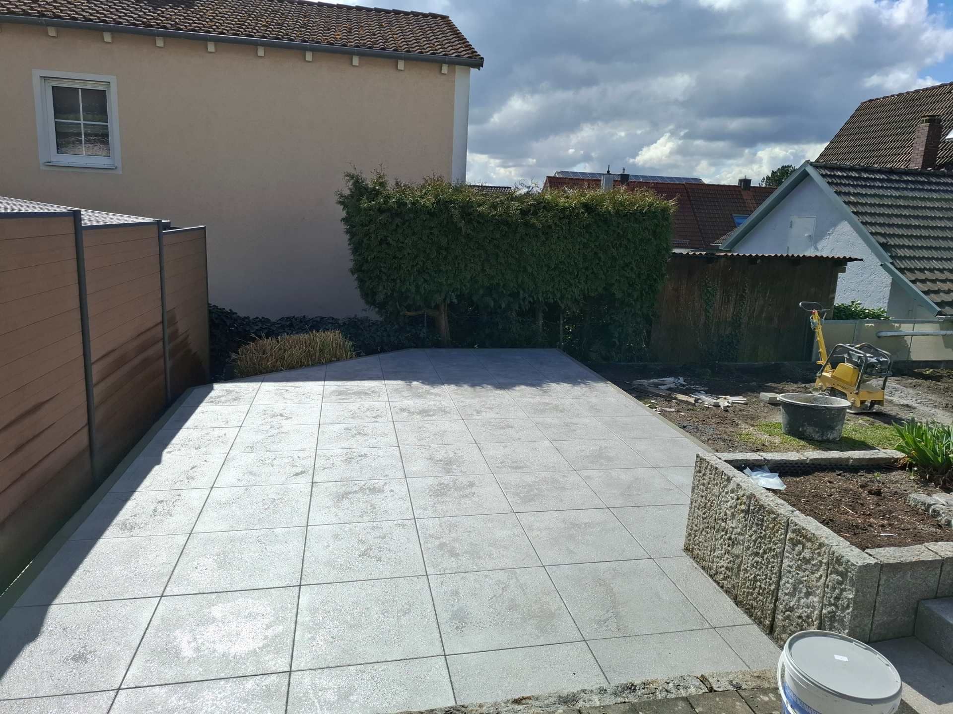 Hellgraue Steinterrasse im Hinterhof mit Zaun, Hecke, Pflanzkasten