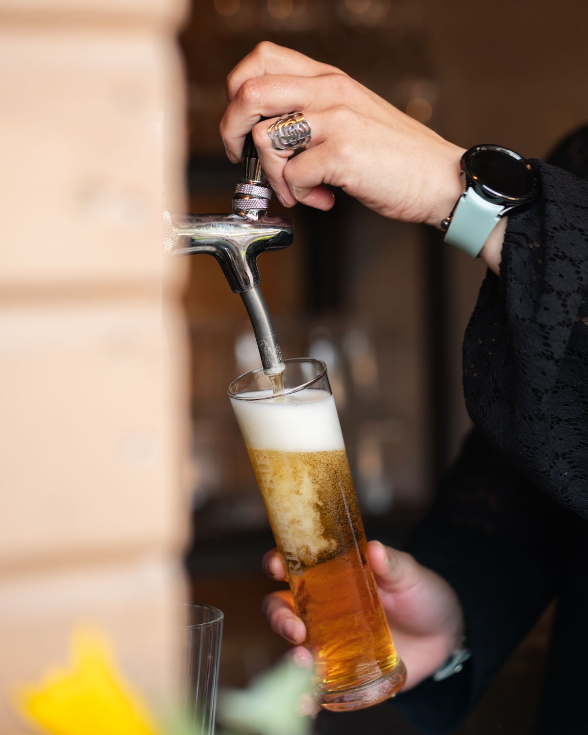 Bier wird von Hand aus dem Zapfhahn in ein schräg gestelltes Glas eingeschenkt, wobei sich eine schaumige Krone bildet.