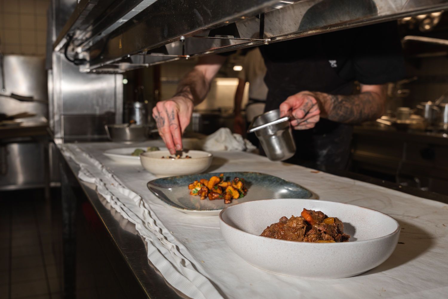 Ein Koch richtet in der Restaurantküche mit einer Zange und einem Saucenbecher Gerichte an.