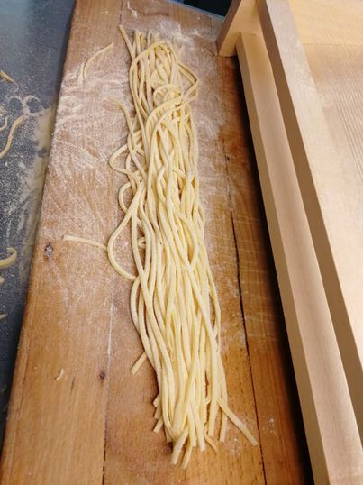 Frisch zubereitete Spaghetti-Nudeln auf einer bemehlten Holzoberfläche neben einem hölzernen Nudeltrockner.