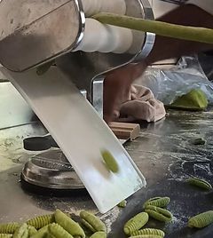 Eine Nudelmaschine presst grüne Nudeln auf eine Oberfläche, im Vordergrund sind fertige Nudeln zu sehen.