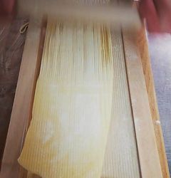 Nudelteig wird mit einem Holzschneider auf einer Holzoberfläche in Nudeln geschnitten.