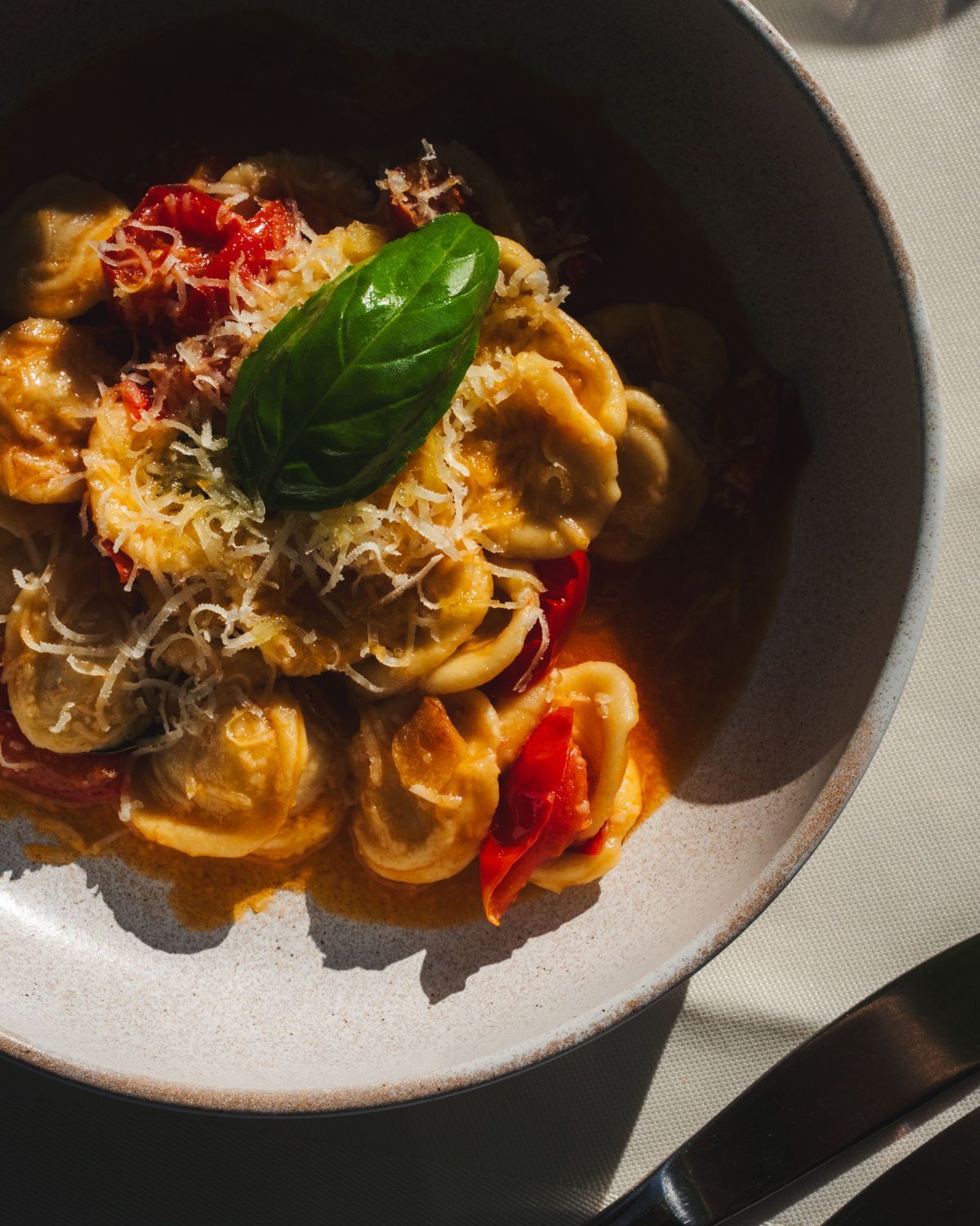 Eine Schüssel Pasta mit Tomatensoße, geriebenem Käse und Basilikum, beleuchtet von warmem Sonnenlicht.
