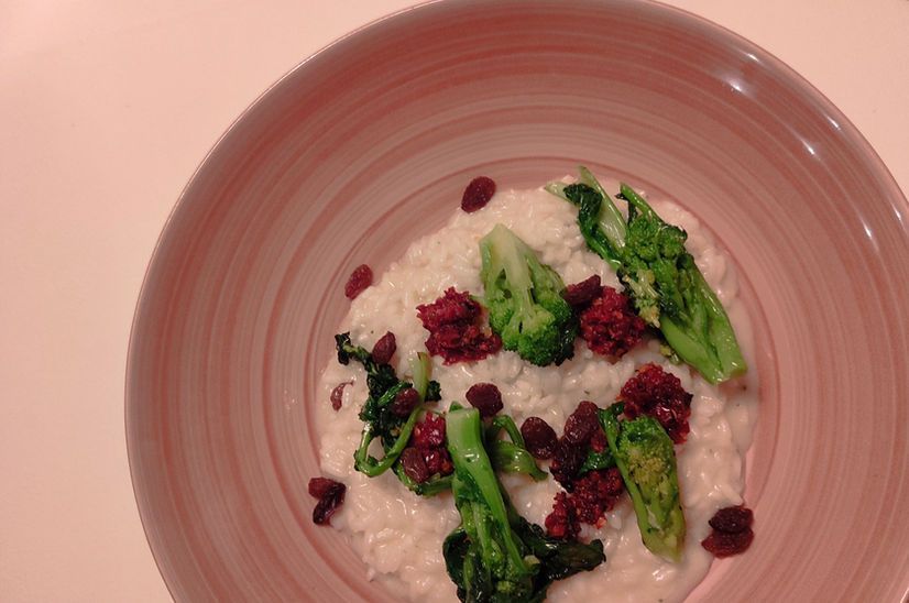 Cremiges Risotto in einer rosa Schüssel, garniert mit grünem Brokkoli, roten Preiselbeeren und einem roten Relish.