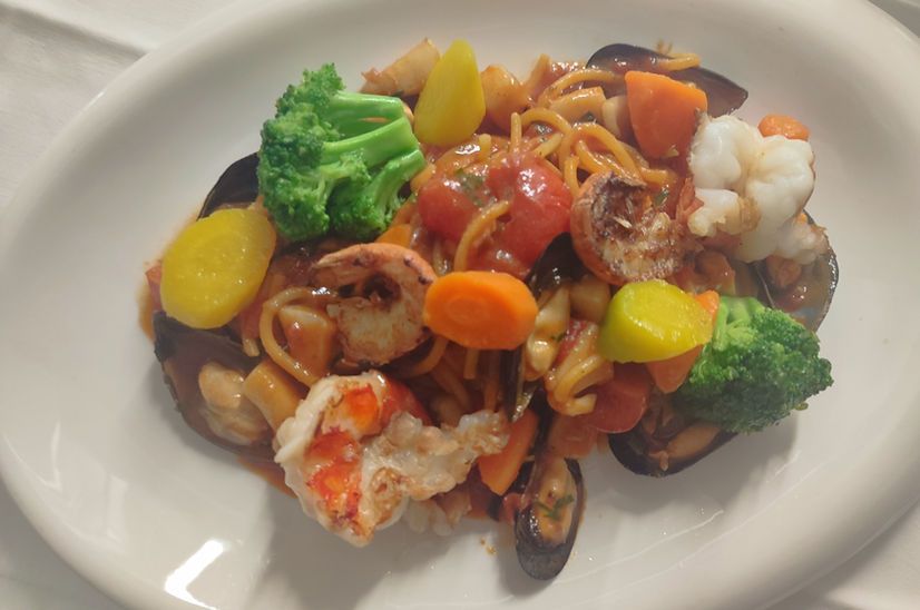 Nudelgericht mit Garnelen, Muscheln, Brokkoli, Karotten und Tomaten.