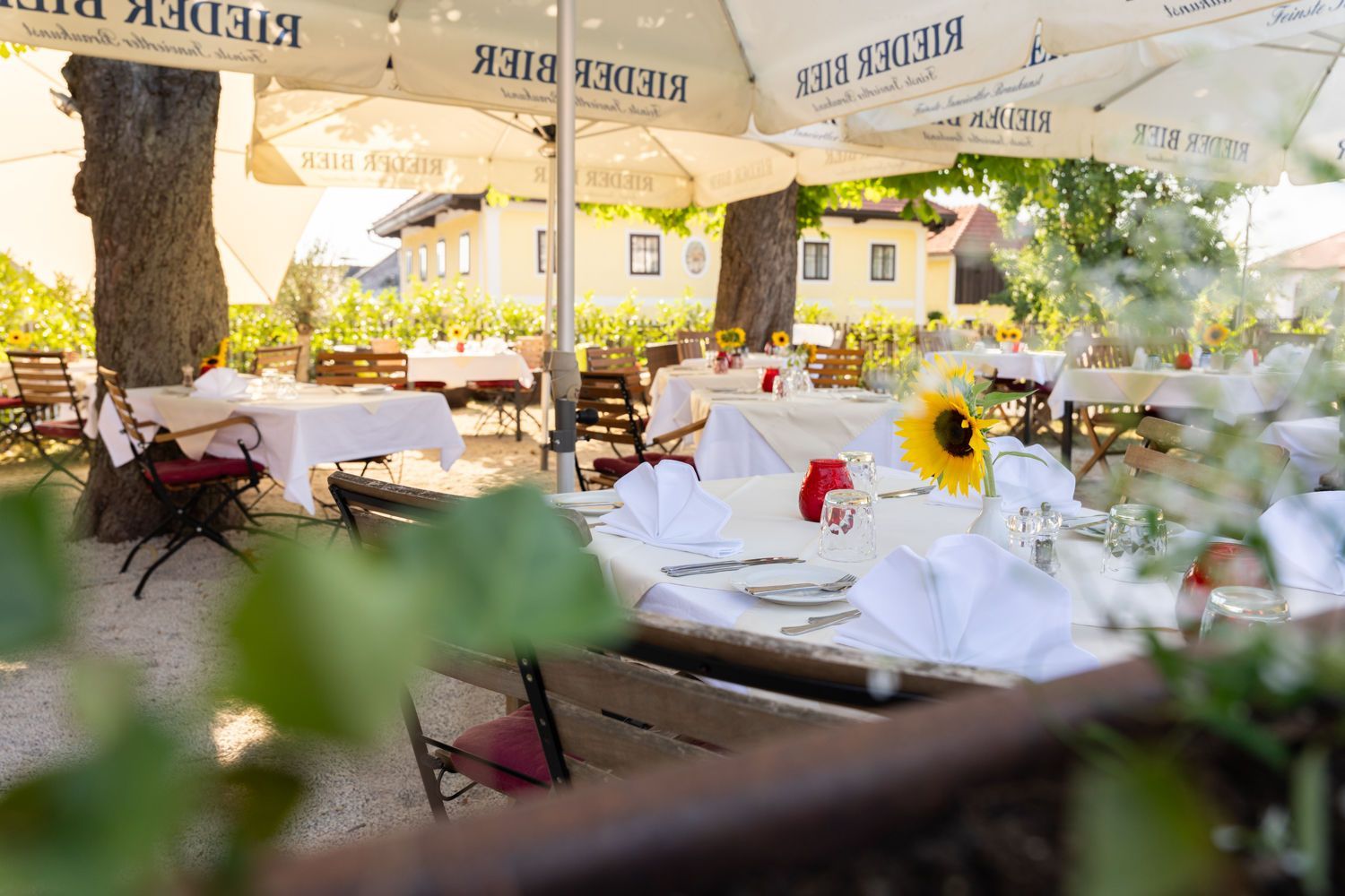 Terrasse eines Cafés im Freien mit weißen Tischdecken, Sonnenschirmen und blumengeschmückten Tischen im warmen Sonnenlicht