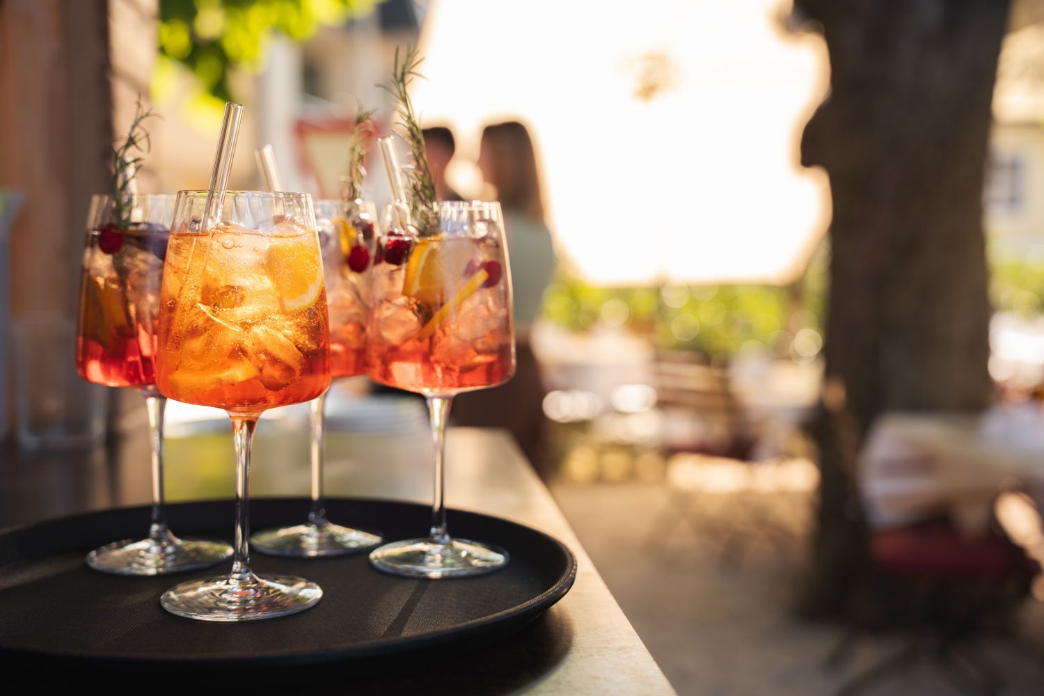 Drei Weingläser mit Orangensaft und Eis auf einem Tablett im Freien in der warmen Sonne