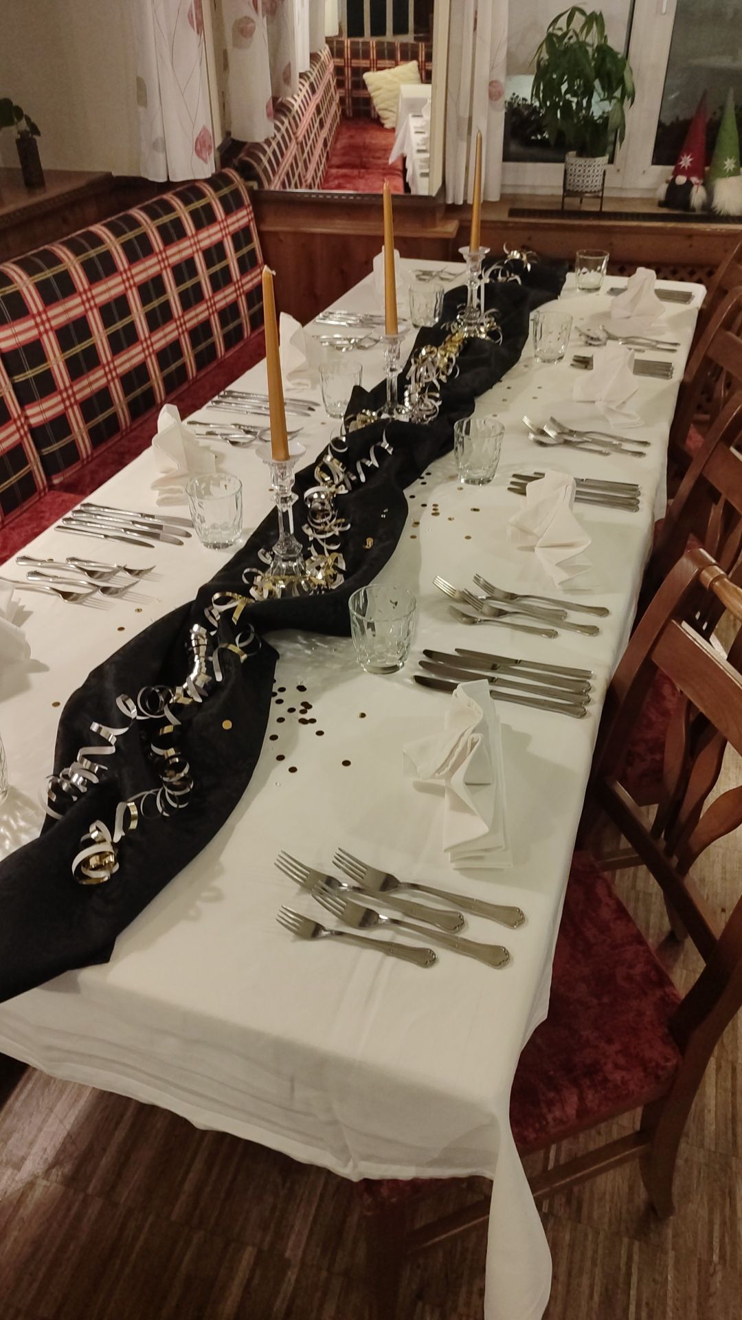 Langer Tisch, gedeckt für ein formelles Abendessen mit schwarzem Tischläufer, Kerzen, Besteck und Dekorationen.