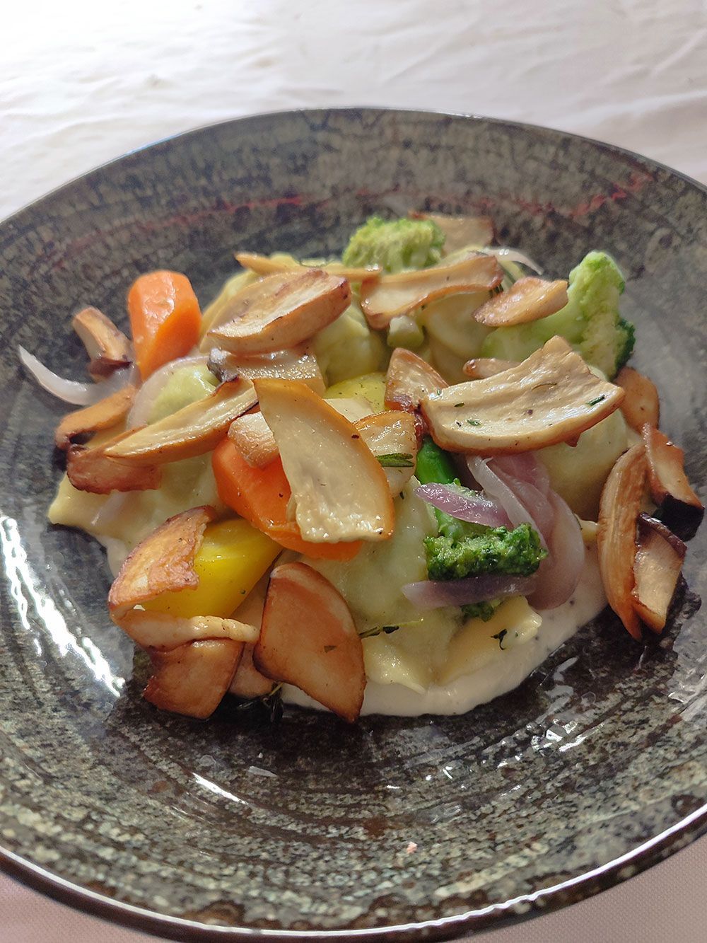 Gemüse- und Pilzgericht in einer grauen Schüssel. Zu den Gemüsesorten gehören Karotten, Brokkoli und Zwiebeln.