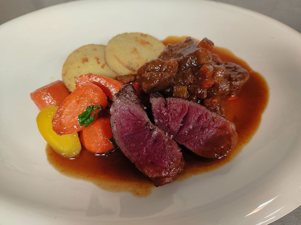 Teller mit geschmortem Fleisch, Wurzelgemüse und Kartoffelscheiben in reichhaltiger Soße.