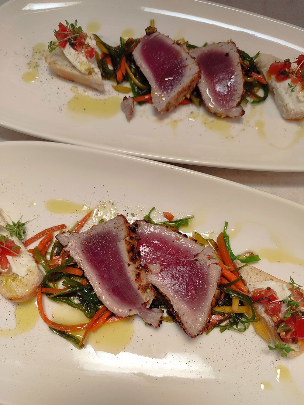 Gebratenes Thunfischsteak mit Gemüse und Bruschetta auf einem weißen Teller.