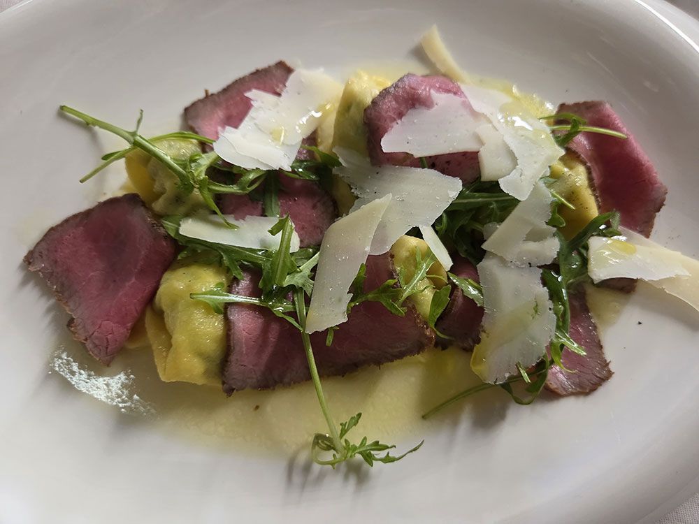 Rindfleischscheiben mit Nudeln, Rucola, Parmesan und Soße auf einem weißen Teller.