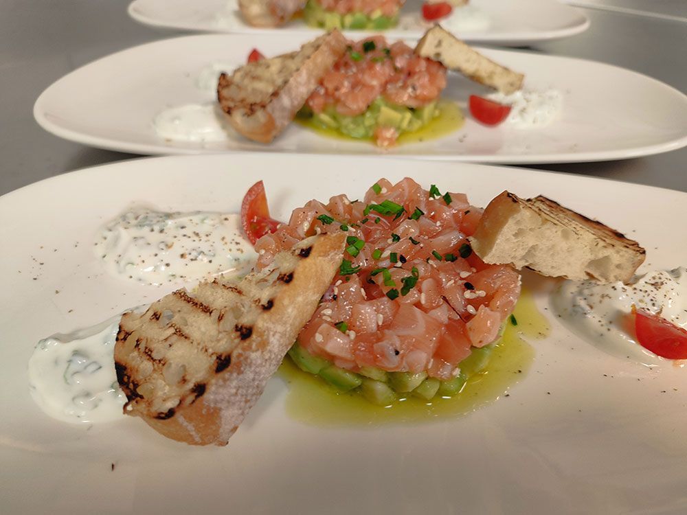 Lachs-Avocado-Tartar mit gegrilltem Brot und Sauce auf einem weißen Teller.