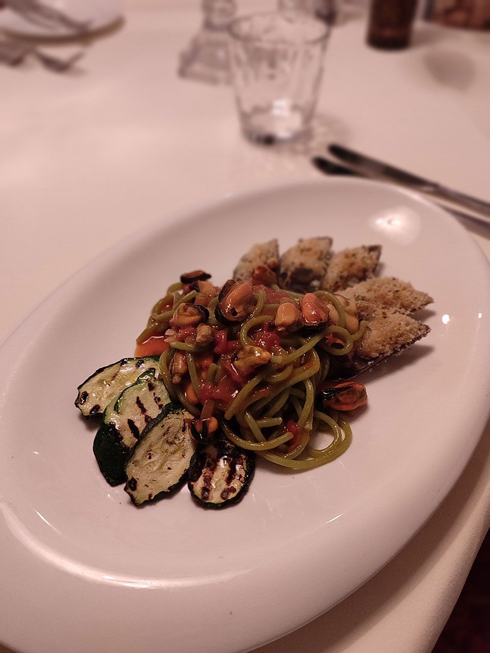 Ovaler Teller mit Nudeln, gegrillten Zucchini und paniertem Essen auf einer weißen Tischdecke.