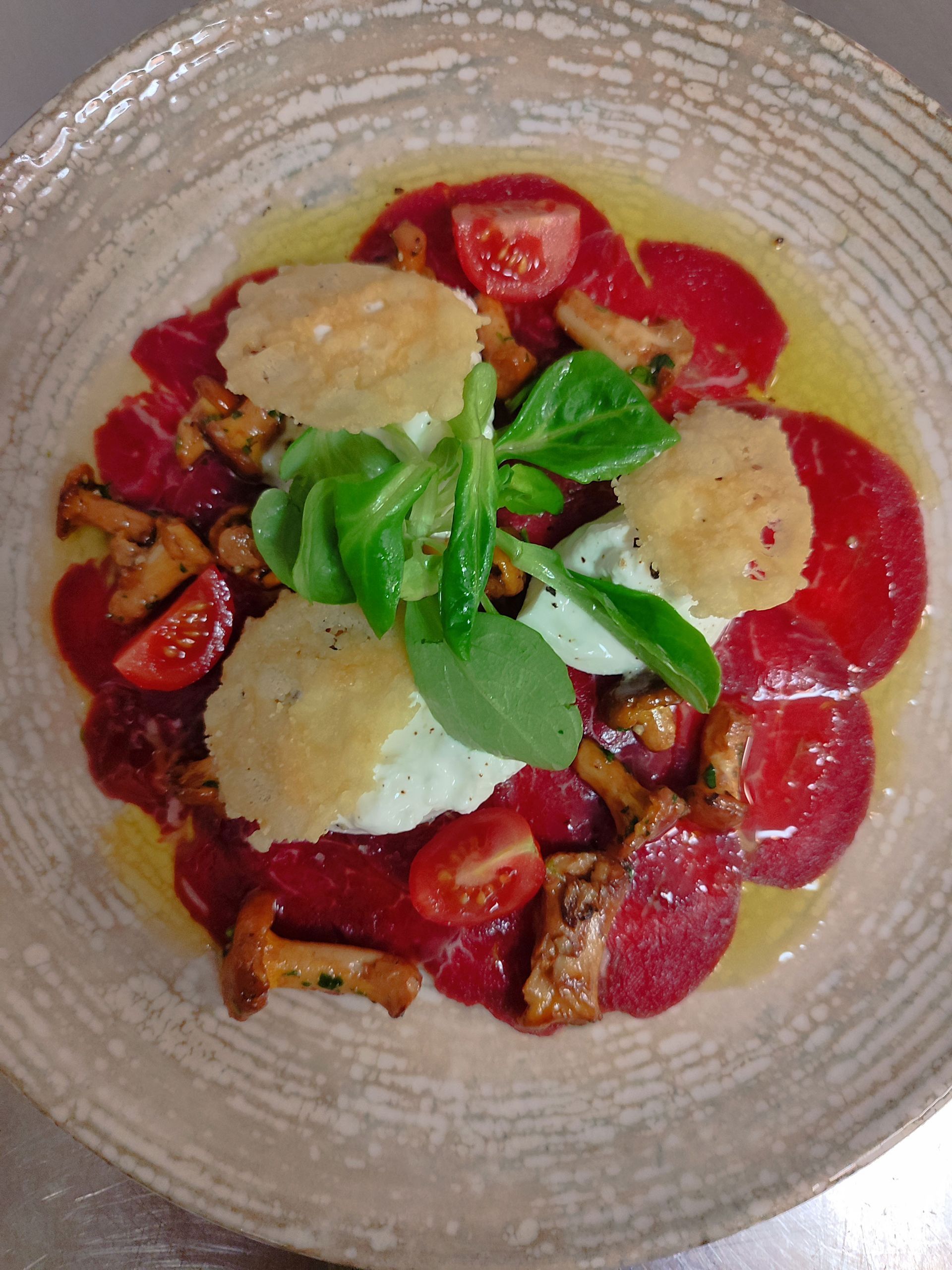 Dünn geschnittenes rotes Fleisch mit Pilzen, Tomaten, Käsechips und Gemüse in einer flachen Schüssel.