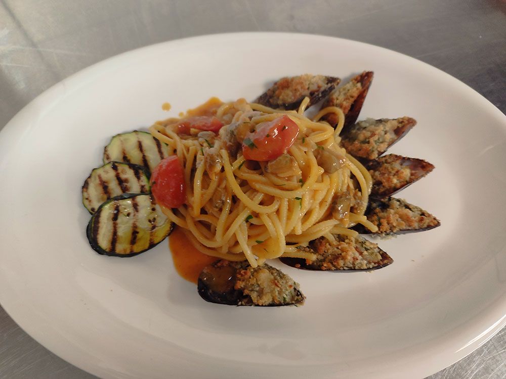 Spaghetti mit Tomaten, gegrillten Zucchini und gebackenen Muscheln auf einem weißen Teller.