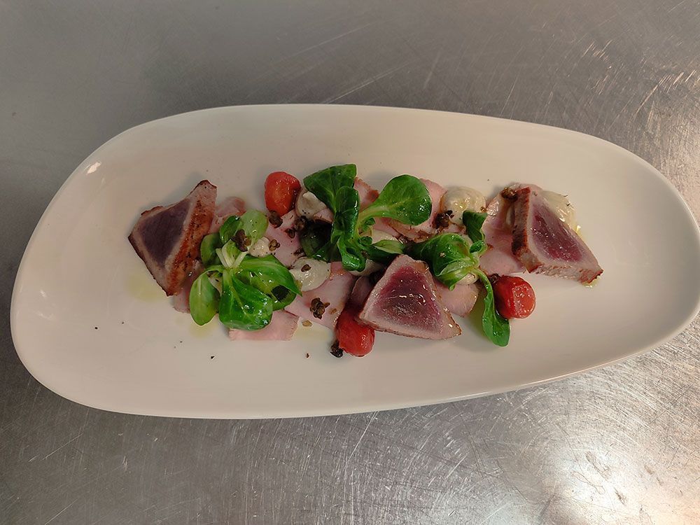 Gebratener Thunfisch mit Gemüse, Tomaten und Soße auf einem weißen ovalen Teller.