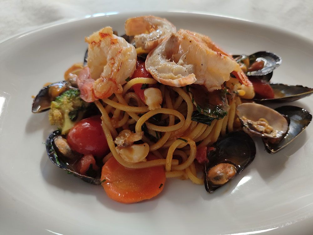 Meeresfrüchte-Pasta mit Garnelen, Muscheln, Tomaten, Brokkoli und Karotten auf einem weißen Teller.