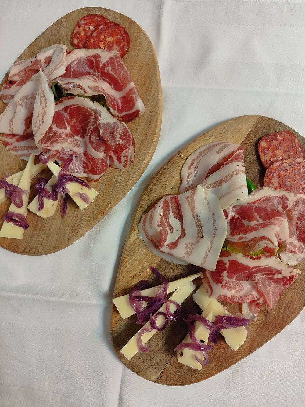 Zwei hölzerne Servierbretter mit Wurst und Käse auf einer weißen Tischdecke.