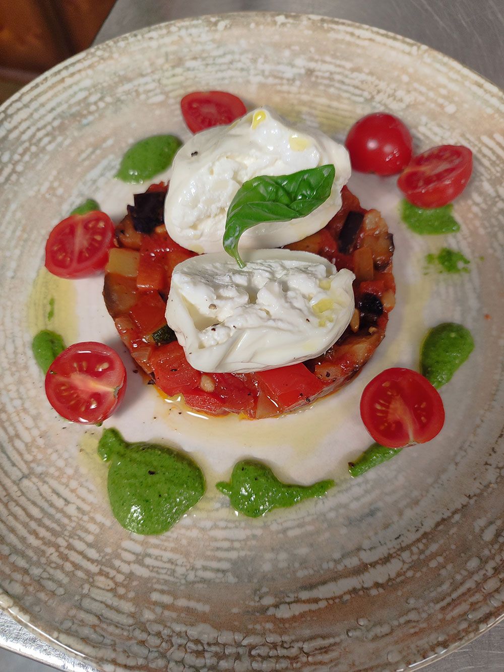 Burrata-Käse mit Tomaten, Basilikum und Pesto auf einem Teller.