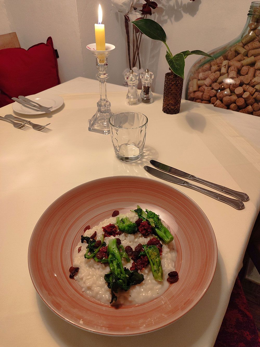 Teller Risotto mit Brokkoli und Preiselbeeren auf einem mit einer Kerze gedeckten Tisch.