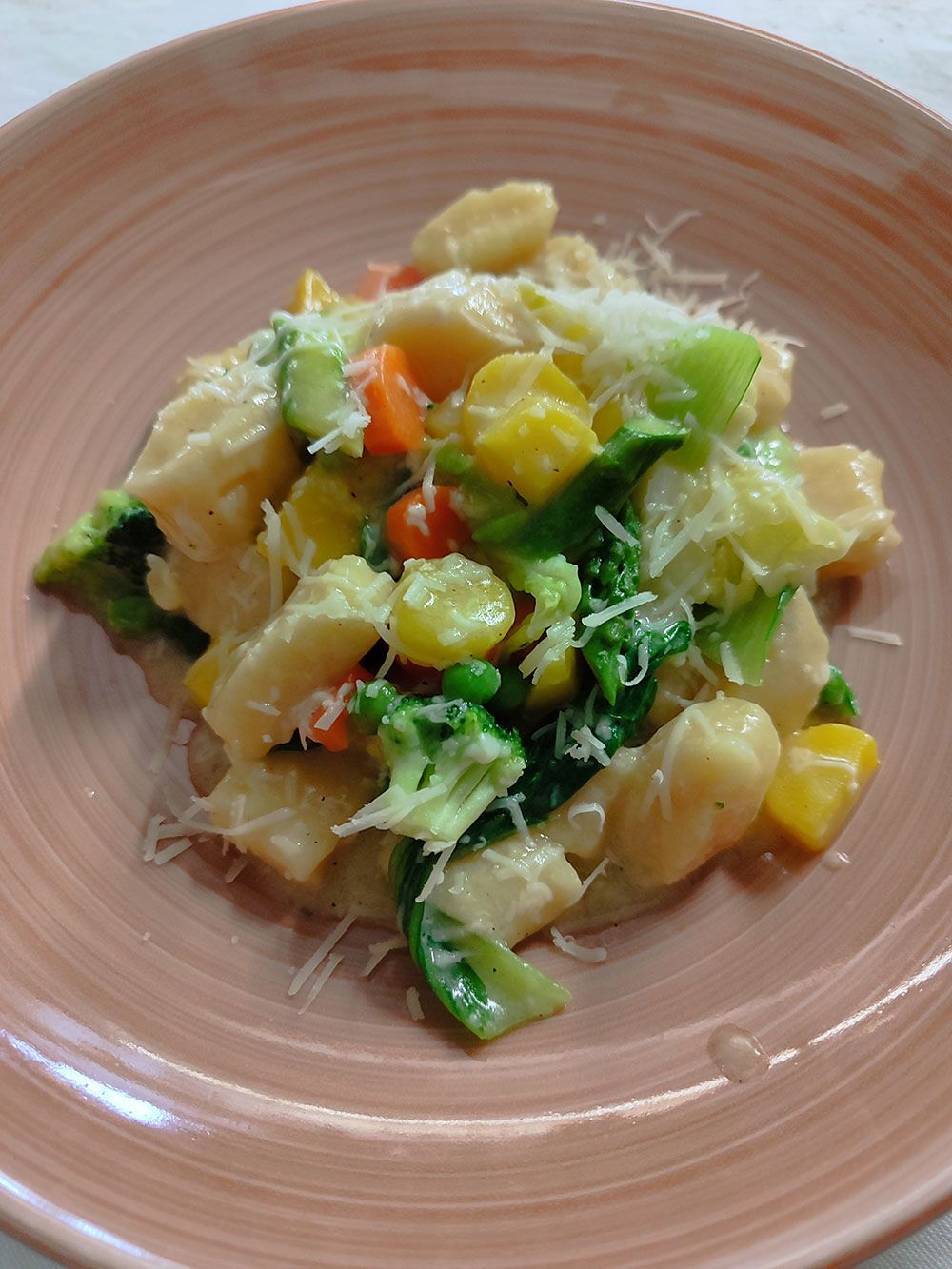 Gnocchi mit gemischtem Gemüse, mit geriebenem Käse bestreut, in einer rosa Schüssel.