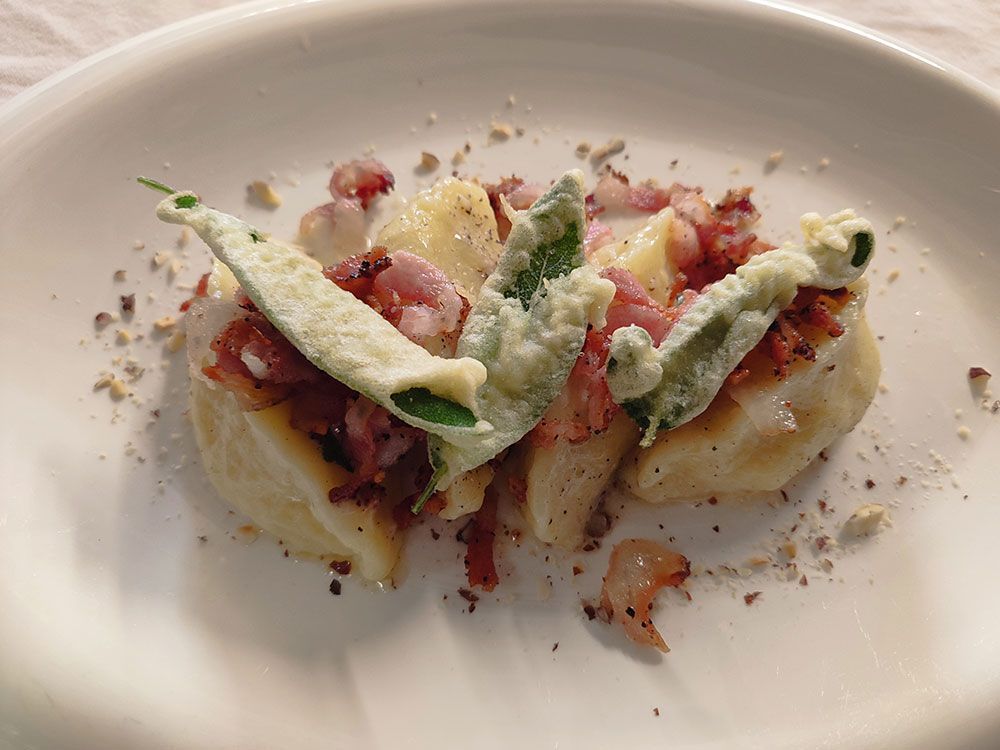 Gnocchi-Gericht mit gebratenen Salbeiblättern, Speckwürfeln und zerstoßenen Nüssen auf einem weißen Teller.