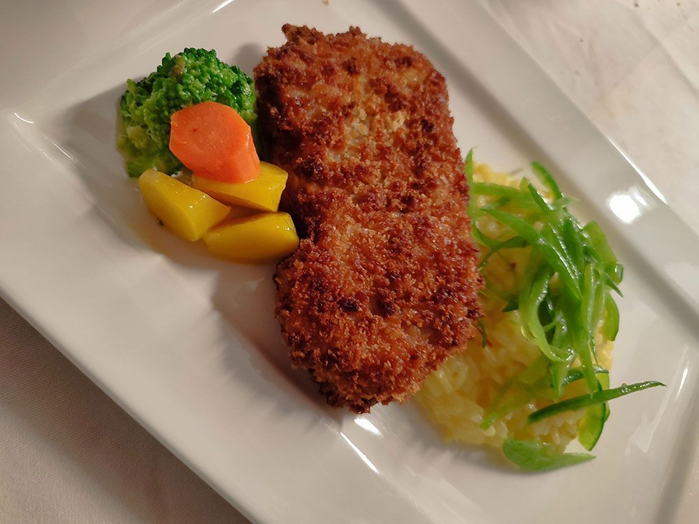 Paniertes und gebratenes Fleisch mit Kartoffelpüree, Brokkoli und Karottenscheiben auf einem weißen Teller.