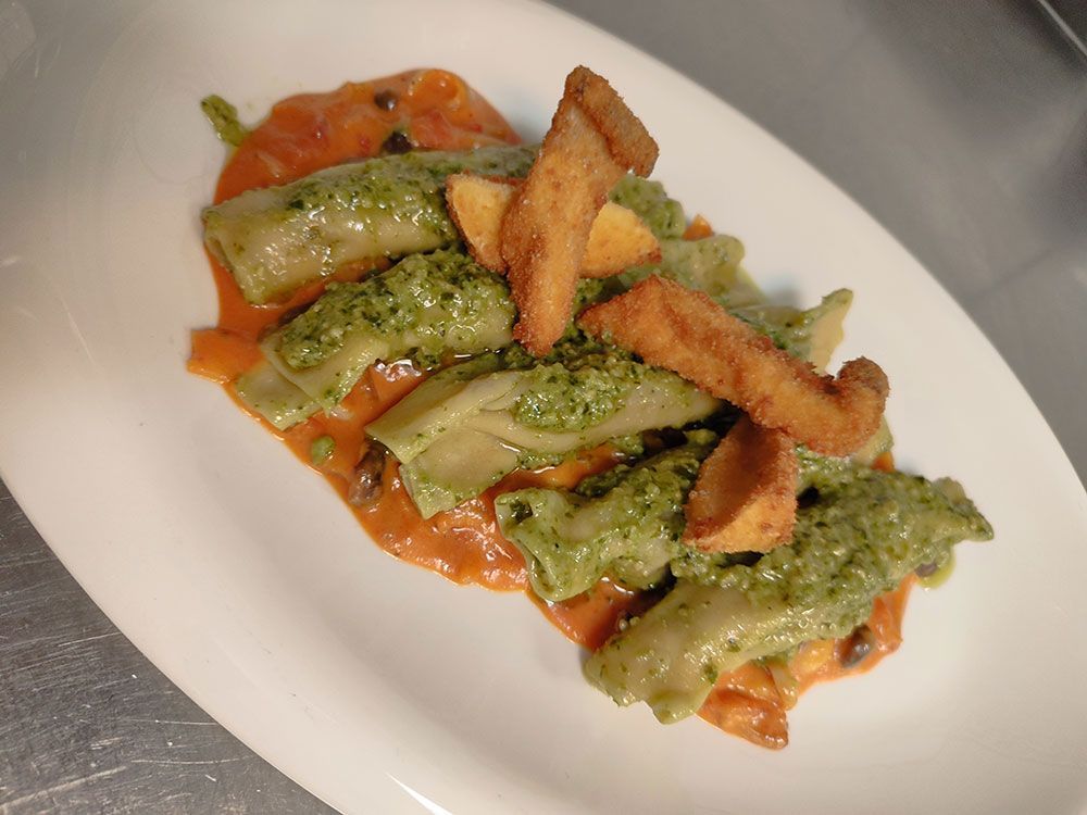 Nudelgericht mit grünem Pesto und frittierten Brotstücken auf Orangensauce.