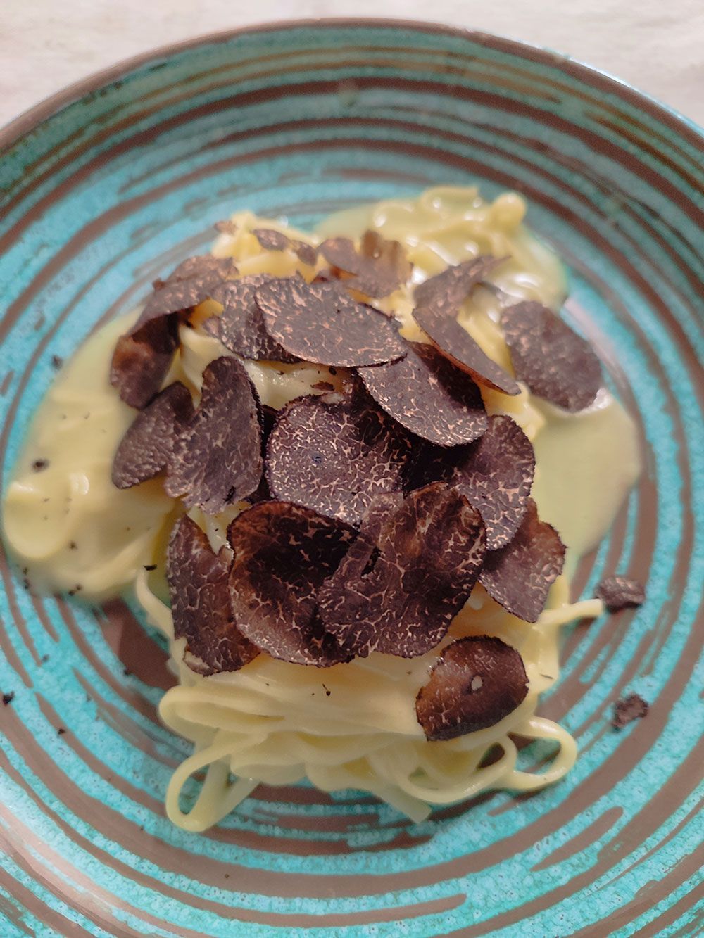 Nudelgericht mit gehobelten schwarzen Trüffeln auf einem türkis-braunen Teller.