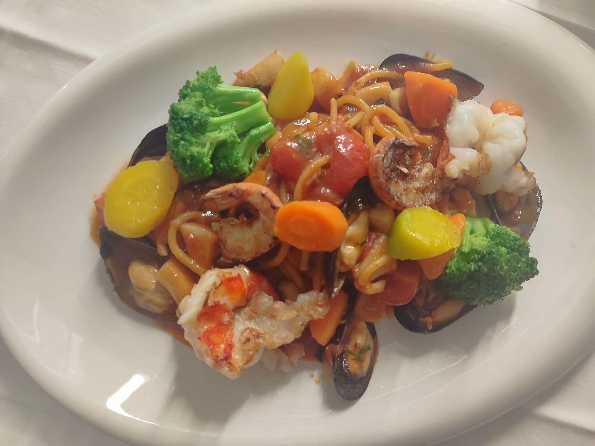 Spaghetti mit Meeresfrüchten und Gemüse in Tomatensoße auf einem weißen Teller.