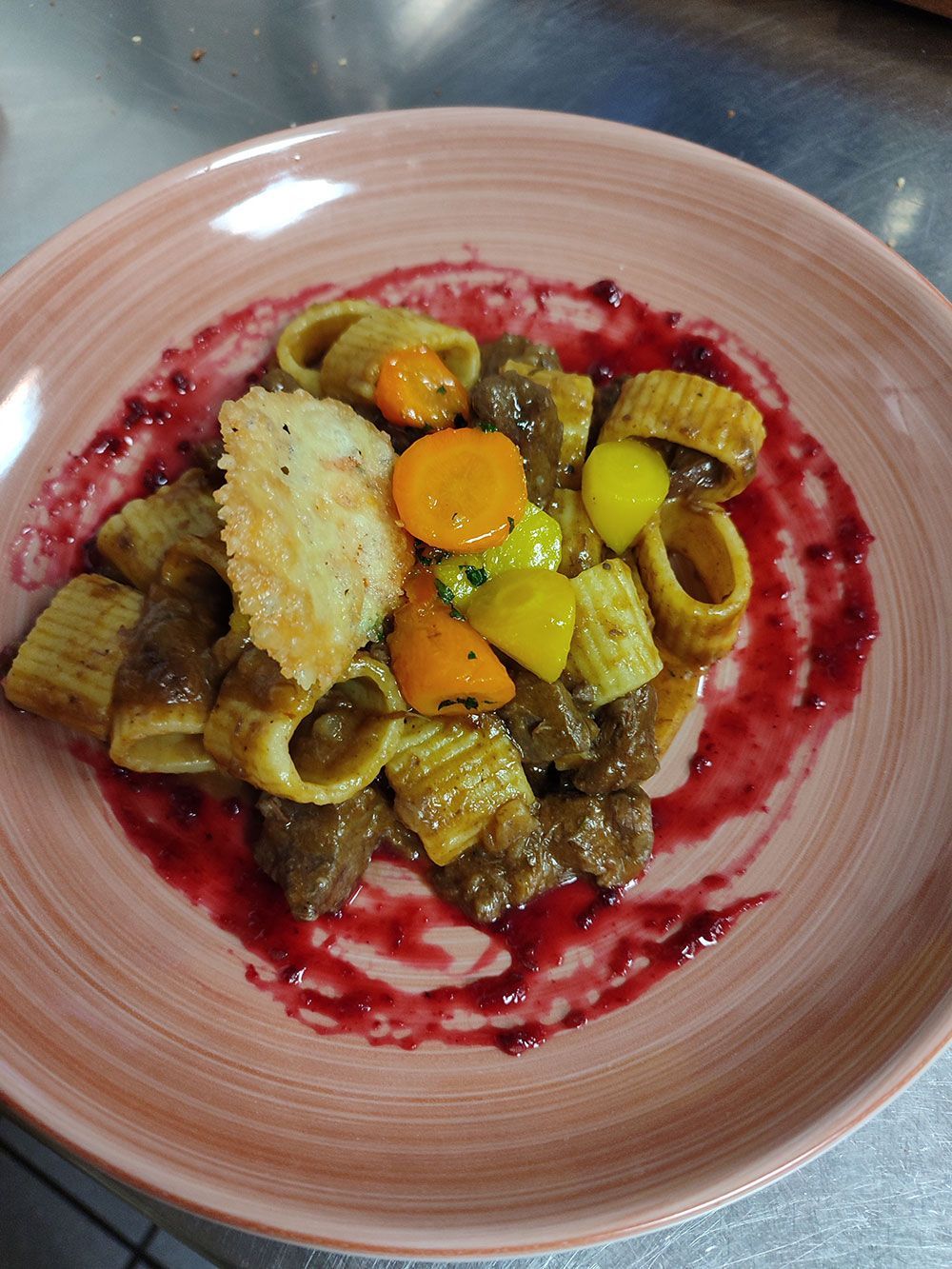 Pasta mit Fleisch und Gemüse, garniert mit einer roten Sauce, serviert auf einem rosa Teller.