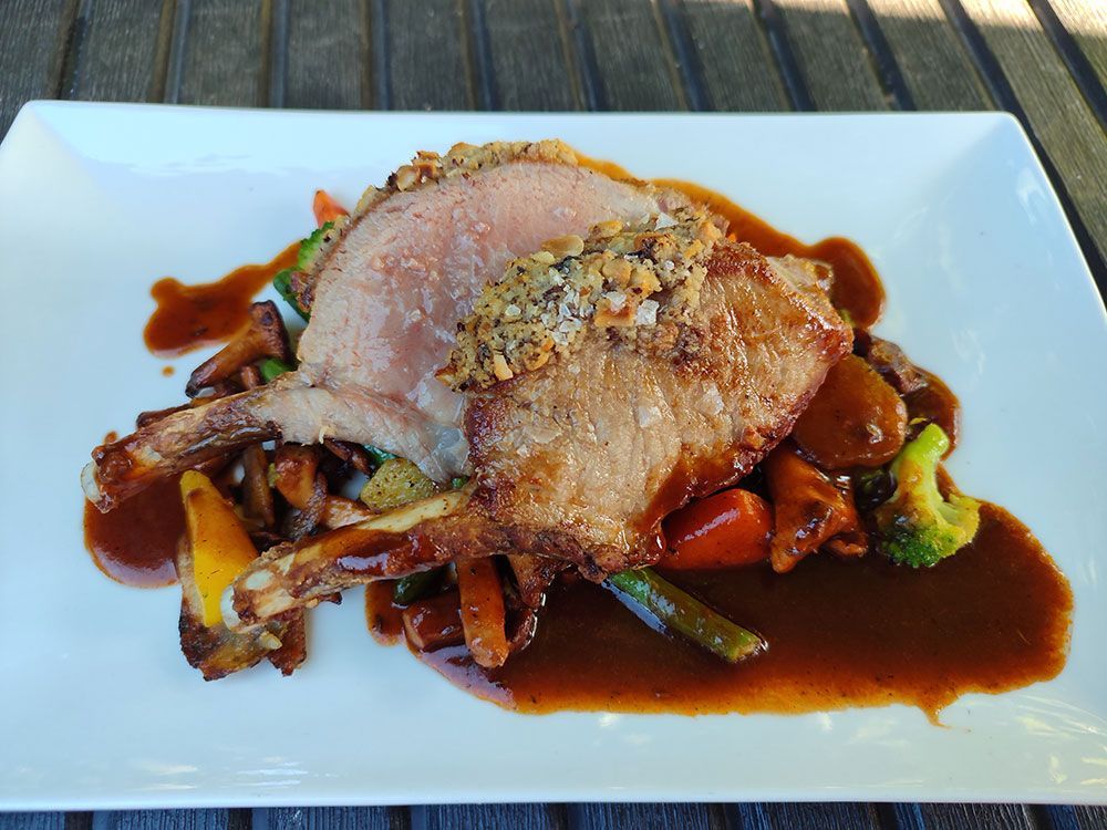 Schweinekotelett mit Nusskruste und Soße, auf geröstetem Gemüse, auf einem weißen Teller.