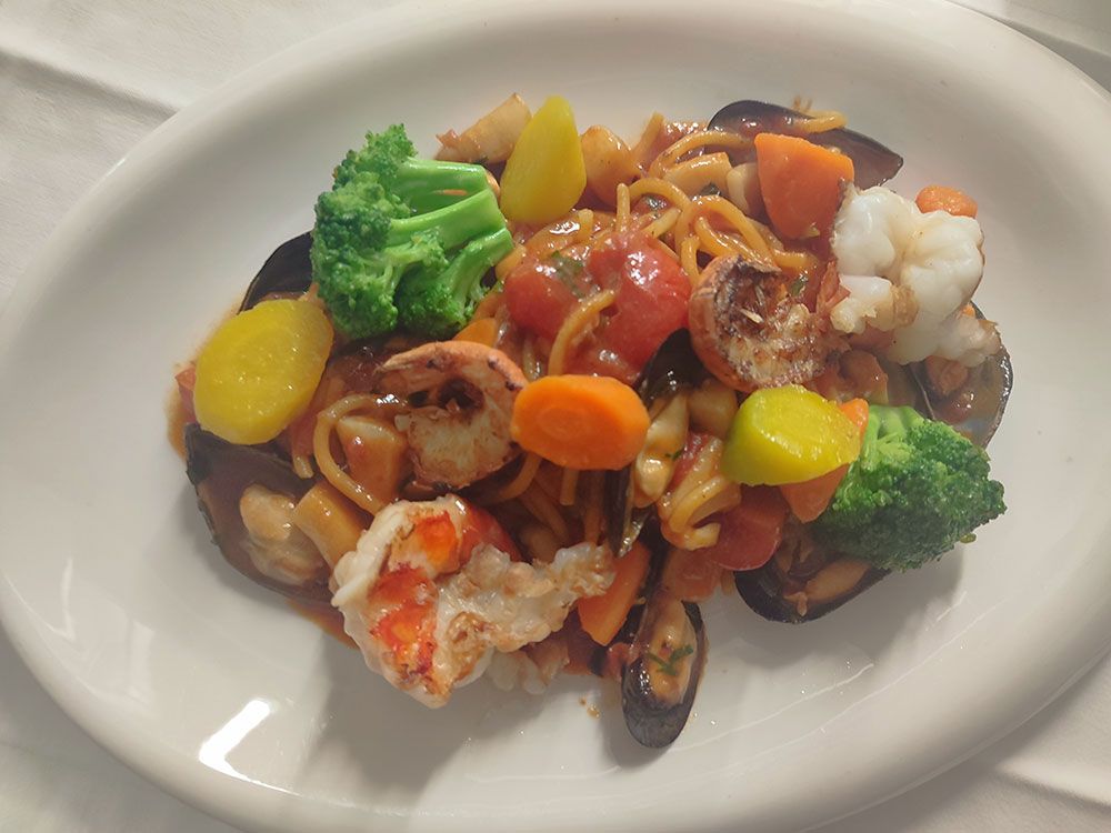 Nudelgericht mit Meeresfrüchten auf weißem Teller; Spaghetti mit Muscheln, Garnelen, Gemüse und Tomatensoße.