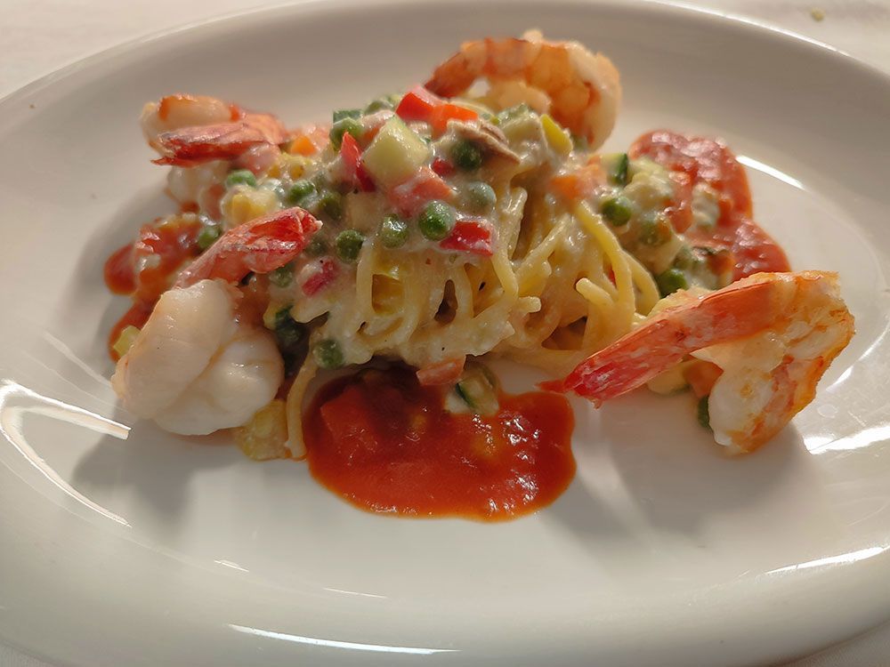 Spaghettigericht mit Garnelen, Erbsen, Paprika und Tomatensoße auf einem weißen Teller.