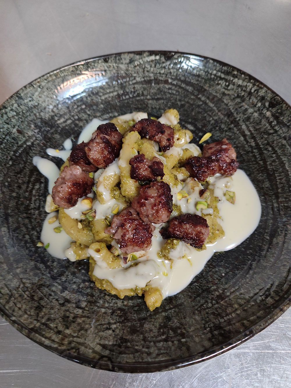 Nudelgericht: Makkaroni mit Fleischbällchen, Sahnesauce und gehackten Pistazien auf einem dunklen Teller.