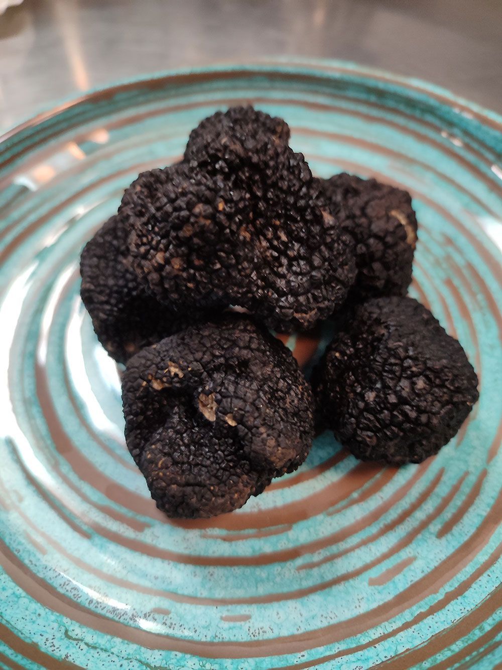 Schwarze Trüffel auf einem türkis-braun gewirbelten Teller.