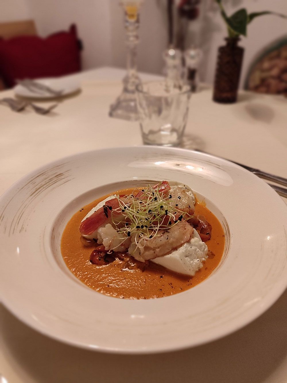 Fischgericht in Orangensauce auf einem weißen Teller, auf einer weißen Tischdecke angerichtet.