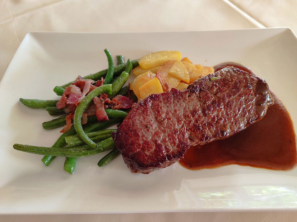 Steak-Dinner: Steak mit Soße, grüne Bohnen mit Speck und Kartoffeln auf einem weißen Teller.