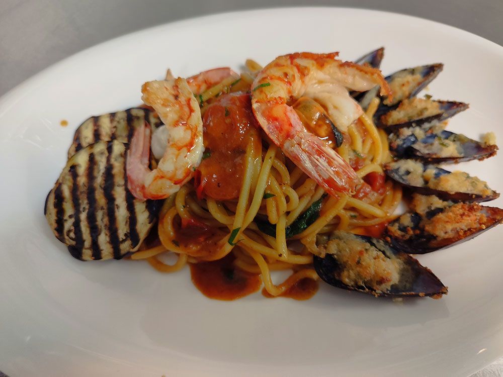 Spaghettigericht mit Garnelen, Muscheln und gegrillter Aubergine auf einem weißen Teller.