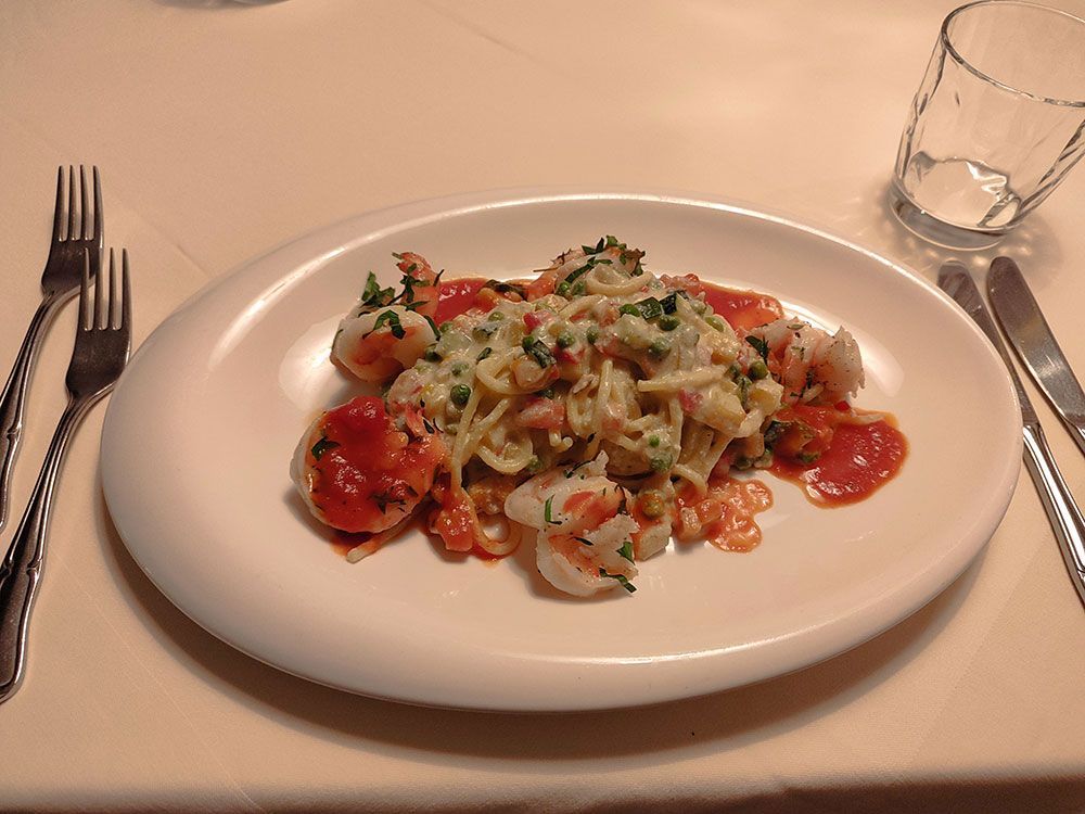 Nudelgericht mit Garnelen und Tomatensoße auf einem weißen Teller, Besteck und Wasserglas.