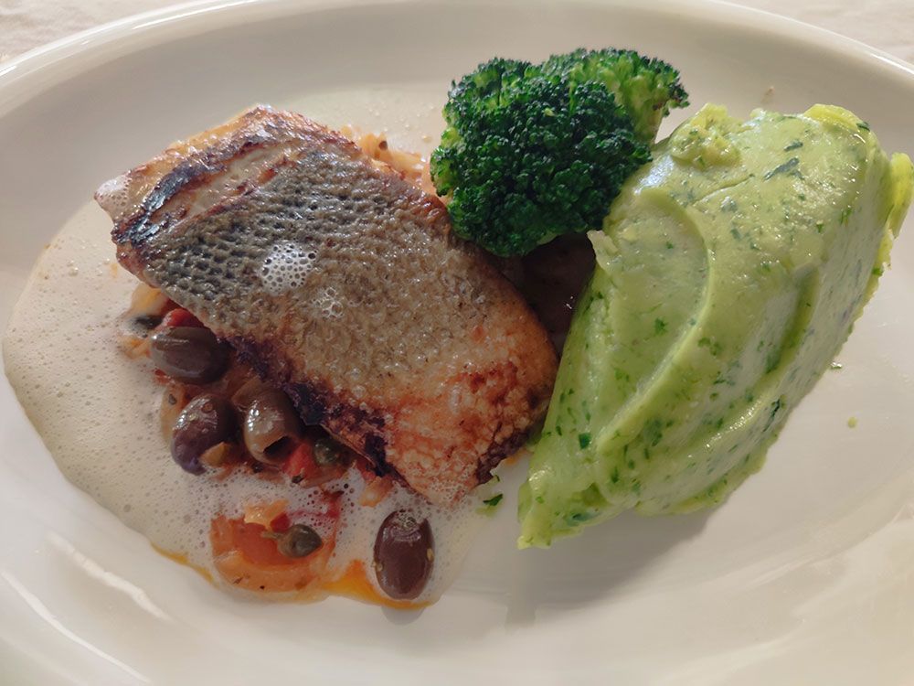 In der Pfanne gebratener Fisch auf einem Gemüsebett, serviert mit Brokkoli und grünem Kartoffelpüree auf einem weißen Teller.