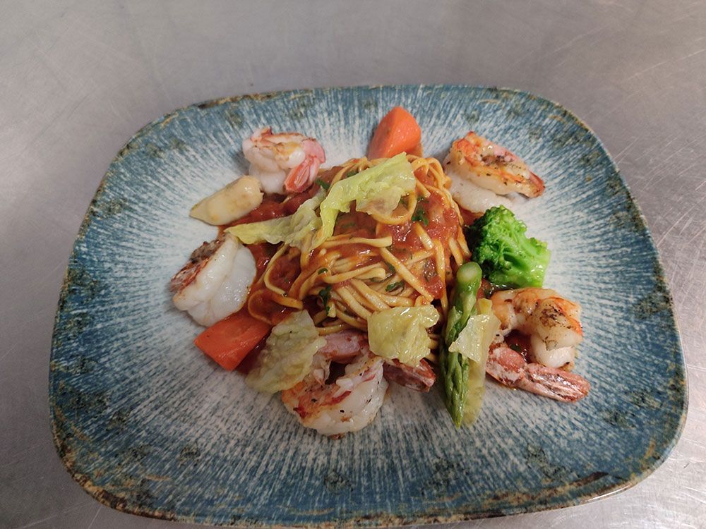 Nudelgericht mit Garnelen, Brokkoli, Spargel und Karotten auf einem blauen Teller.