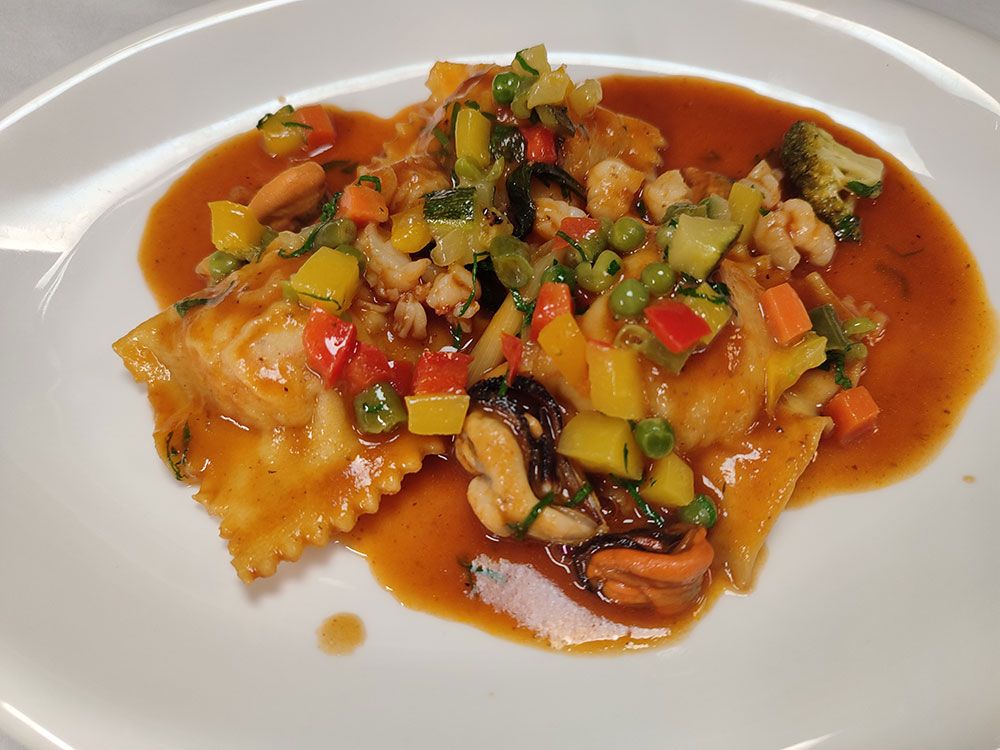 Ravioli mit Meeresfrüchten, Gemüse und Sauce auf einem weißen Teller.